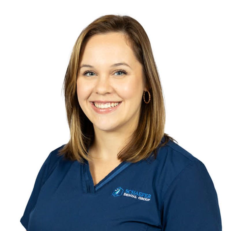 Smiling female team member in Schaefer Dental Group scrubs, East Lansing dental clinic, plain white background.