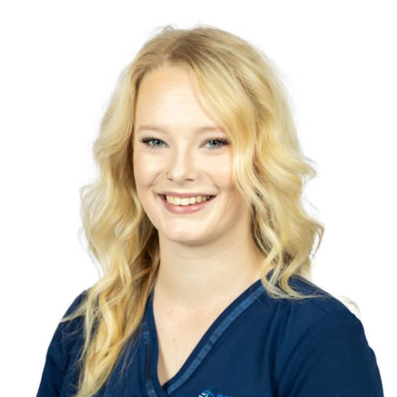 Smiling woman with long, wavy blonde hair in a navy top, relaxed as at an East Lansing dentist; white background.