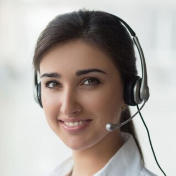 Receptionist with dark hair wearing a headset, smiling at front desk of a dental clinic in East Lansing, Michigan.